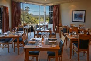 un restaurante con mesas y sillas de madera y ventanas en Distinction Fox Glacier - Te Weheka Boutique Hotel, en Fox Glacier