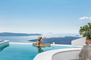 a woman in a hat sitting in a swimming pool at Anteliz Suites in Fira