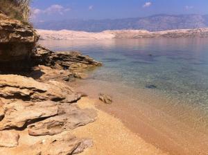 a beach with rocks and the water and mountains at Bara Bay in Metajna