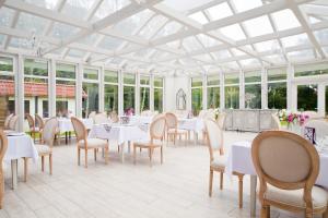 a conservatory with white tables and chairs and windows at Dworek Bukowy Park in Szczecin