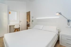 a white bedroom with a white bed and a lamp at Apartaments Cales de Ponent in Ciutadella