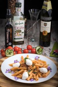 une assiette de pâtes et de légumes sur une table avec des bouteilles de vin dans l'établissement Apartments O Sole Mio, à Vukovar