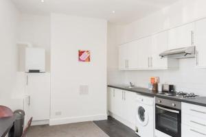 a kitchen with white cabinets and a washer and dryer at Kennington Apartment A/Apartment in London
