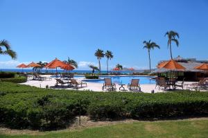 a pool with chairs and umbrellas and the ocean at Condominios Ballena in Cabo San Lucas