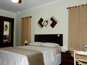 1 dormitorio con 1 cama con sábanas blancas y fotografías en la pared en Pousada Apricare, en Cabo Frío