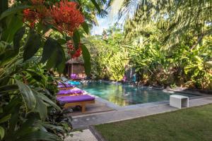 a pool with a row of chaise lounges next to a garden at Arjuna Homestay in Pemuteran