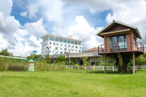 a house in a field with a building in the background at Prajaktra Design Hotel in Udon Thani