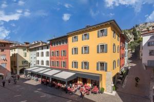 une vue sur un grand bâtiment jaune avec des tables dans l'établissement Hotel Centrale, à Nago-Torbole