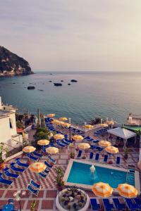 a swimming pool with umbrellas and chairs and the ocean at Hotel Riva del Sole in Ischia