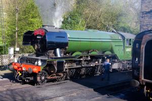 a green train on the tracks with a man walking next to it at The Fleece Inn in Haworth