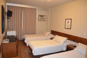 a hotel room with three beds and a television at Niteroi Palace Hotel in Niterói