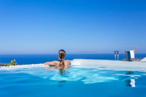 una mujer en una piscina con el océano en el fondo en Amber Light Villas, en Imerovigli