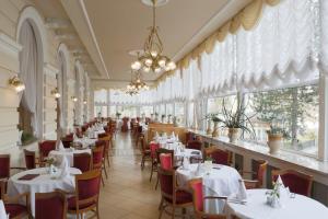 un restaurante con mesas y sillas blancas y ventanas en Hotel Bristol, en Karlovy Vary