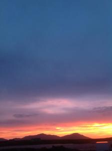 einen Sonnenuntergang am Himmel mit Bergen im Hintergrund in der Unterkunft Uist Travel Accommodation in Daliburgh