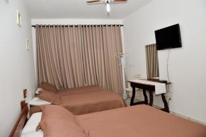 a room with two beds and a desk and a television at Pousada Victor in Ribeirão Claro