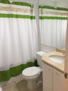 baño con aseo blanco y cortina de ducha verde en Departamento en la Playa, en Algarrobo