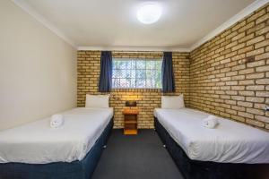 two beds in a room with a brick wall at Caboolture Motel in Caboolture