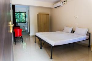 ein Krankenhausbett in einem Zimmer mit einem roten Stuhl in der Unterkunft Lazy Frog Guest House in Cavelossim