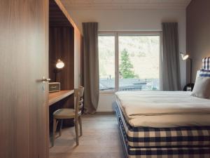a hotel room with a bed and a desk and a window at OVERLOOK Lodge by CERVO Zermatt in Zermatt