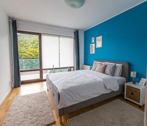 a blue bedroom with a bed and a large window at Tampa Gardens - Mountain View Apartment in Braşov