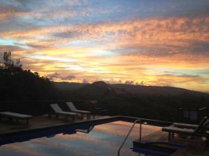 a pool with chairs and a sunset in the background at Santosha Barbados in Saint Andrew