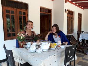 Duas mulheres sentadas numa mesa com comida. em Danara Homestay em Sigiriya