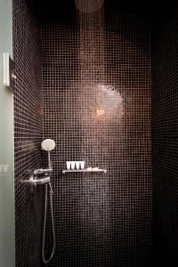 un bagno piastrellato nero con doccia e soffione di Regina Mare-Adults Only Hotel a Imerovigli