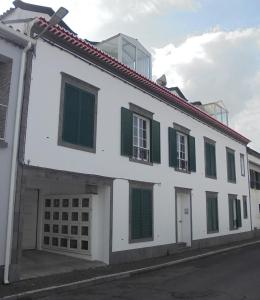 a white building with green shuttered windows on a street at Apartamento Silveira in Furnas