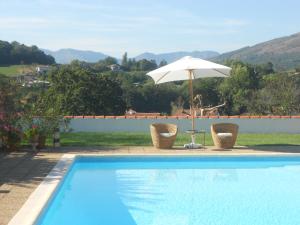 a pool with an umbrella and two chairs and a table with an umbrella at Hôtel Camou in Uhart-Cize