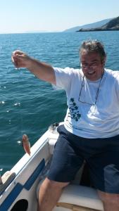 a man sitting on a boat holding a fish at Remezzo Guesthouse in Agios Ioannis Pelio