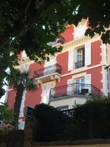 a red building with balconies and a palm tree at Hôtel & Espace Bien-être La Maison du Lierre in Biarritz