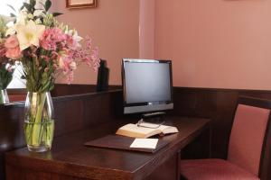 a desk with a vase of flowers and a computer monitor at Hotel City in Piacenza