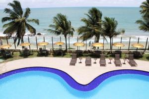 a resort with a pool and chairs and umbrellas and the beach at Praia de Tabatinga- Flat do BZ - 2 quartos in Conde