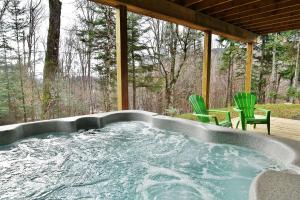 bañera de hidromasaje en un porche con 2 sillas verdes en Chalets Alpins-43 Chemin des Skieurs, en Stoneham