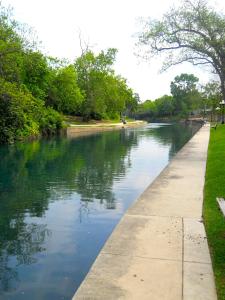 a river with trees and a sidewalk next to the water at River Run Retreat in New Braunfels