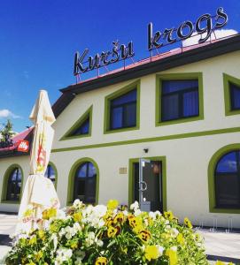 un bâtiment avec un parasol et des fleurs devant lui dans l'établissement Kuršu krogs, à Dižstende