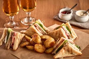 a sandwich and potatoes on a plate with two glasses of beer at Poseidon of Paros Hotel & Spa in Chrissi Akti