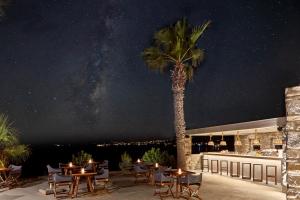 a palm tree on a patio with tables and chairs at Poseidon of Paros Hotel & Spa in Chrissi Akti