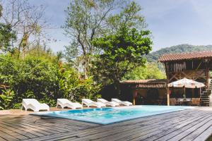 a pool with chairs and an umbrella on a wooden deck at Chalés Água de Coco in Boicucanga