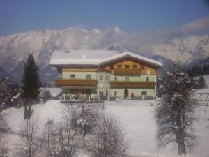 a large building in the snow with a mountain at Gasthof Pension Hetzenbichl in Sankt Johann im Pongau