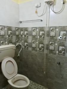 a bathroom with a toilet and a shower with pictures on the wall at Able Homestay in Thekkady
