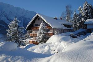 a house covered in snow with trees and snow covered bushes at Hotel Pension Sonnenuhr in Tauplitz