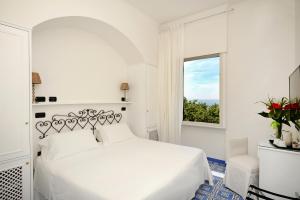 a white bedroom with a white bed and a window at Hotel Aurora in Amalfi