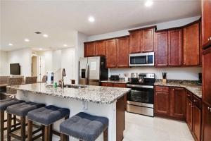 a kitchen with wooden cabinets and a kitchen island with bar stools at DREAM HOUSE, ECOLAB Sanitzed NEAR DISNEY, POOL FENCE in Orlando