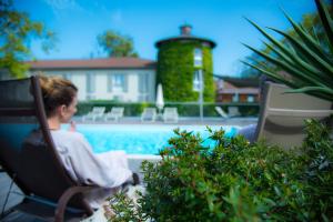 a man sitting in a chair next to a swimming pool at Domaine la Charpinière, The Originals Collection in Saint-Galmier