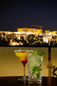 a cocktail and a drink on a table in front of the acropolis at Athens Cypria Hotel in Athens