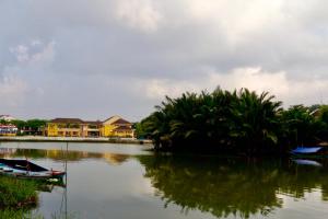 einen Fluss mit Booten, Palmen und Häusern in der Unterkunft Long Life Riverside Hotel in Hoi An