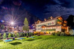 un edificio con panchine in erba di notte di Hotel Villa Rosella Park & Wellness a Canazei