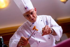 uno chef che tiene in mano una forchetta e un pezzo di cibo di Hotel Villa Rosella Park & Wellness a Canazei Altre 37 foto