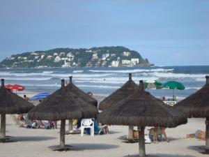 - une plage avec des parasols en paille et des personnes sur la plage dans l'établissement COMFORT GUARUJÁ ENSEADA APARTMENT 26 WIFI, GARAGEM e AR CONDICIONADO, à Guarujá